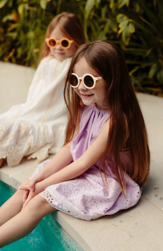 Child sitting by pool wearing the Kids Shades in Bone by Little Drop