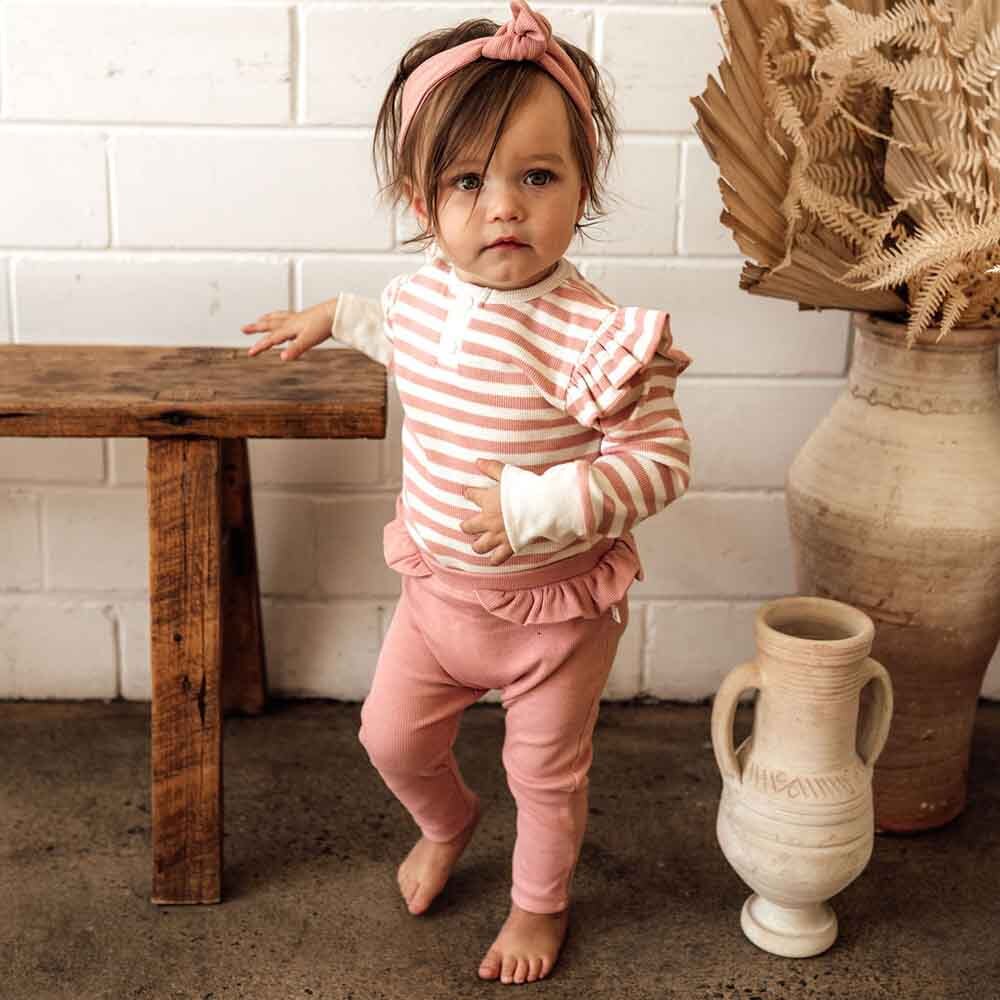 Toddler standing wearing the Rose Stripe Long Sleeve Bodysuit by Snuggle Hunny