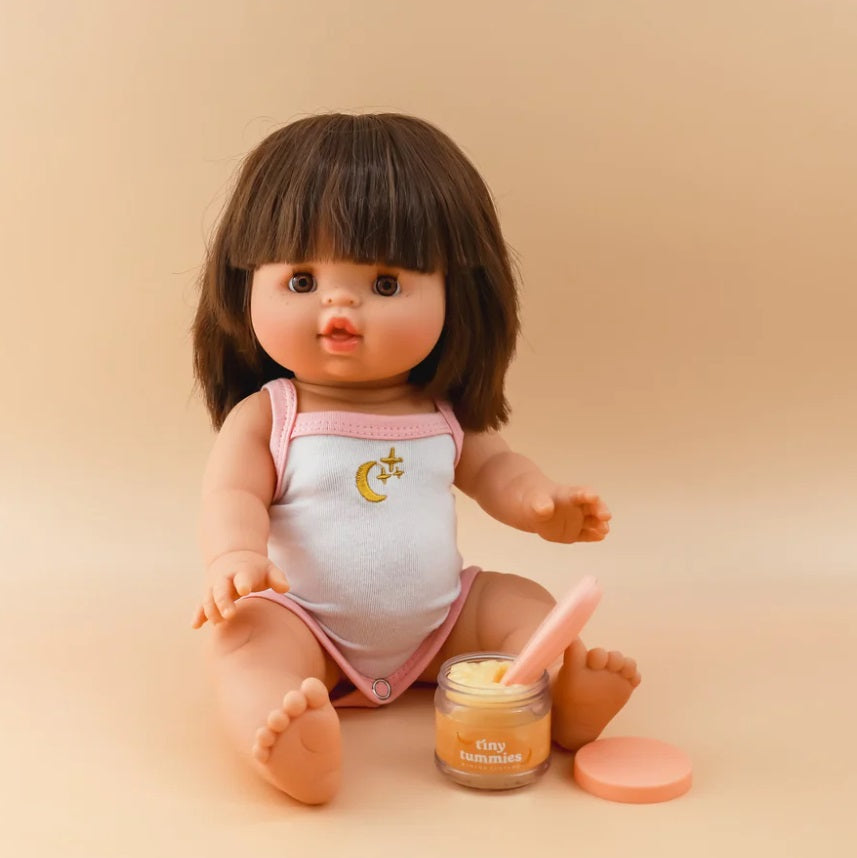 Doll sitting next to the Tiny Tummies Banana Custard by Tiny Harlow